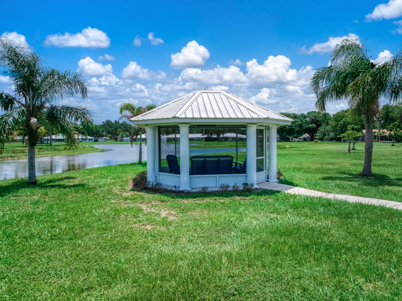 A white gazebo beside the lake between two palms